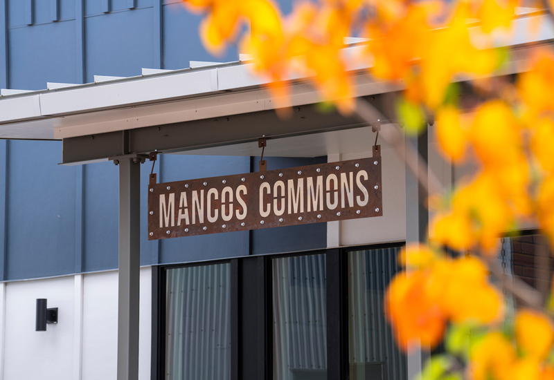 A closeup of the Mancos Commons sign through orange leaves. 