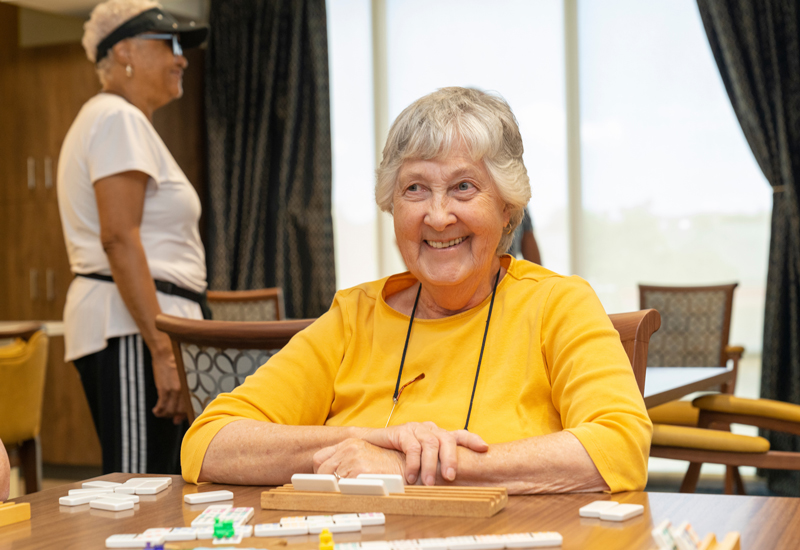 A woman in a yellow shirt playing cards and smiling. 