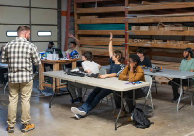 Students sitting at tables with one raising their hand